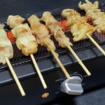 「山善の電気七輪 ESR-Q100 で焼いた焼き鳥。焼き目が付いた美味しそうなねぎま串と鶏皮串が、電気七輪の上でじっくり焼かれている様子。