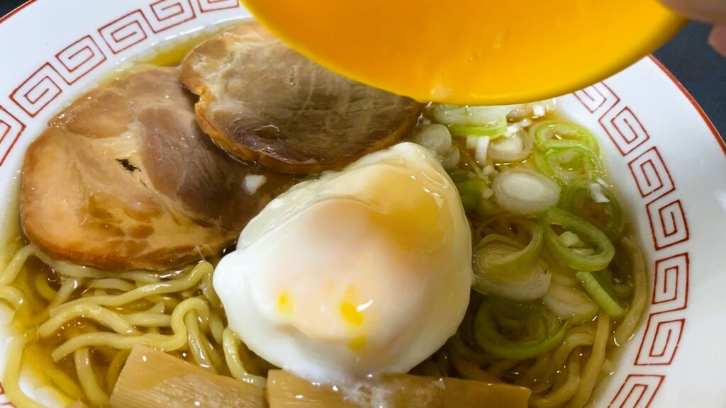 ダイソーの温泉卵調理器で作った温泉卵をラーメンにトッピングしている様子。とろりとした卵が、ラーメンの具材と絡み合って美味しそうな一皿に仕上がっている。