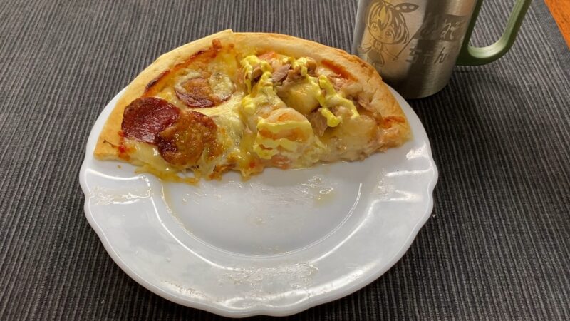 白い皿に乗せられた食べかけの自家製ピザ。マヨネーズがかかっており、横にはキャラクター入りのステンレスマグカップが見える。