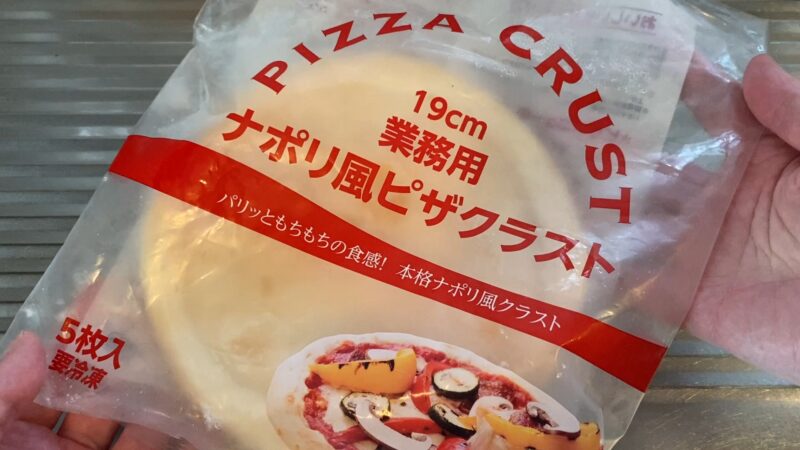 「業務スーパーの『ナポリ風ピザクラスト』パッケージ。5枚入りで、赤い帯に“パリッともっちりの食感!”と記載されている。