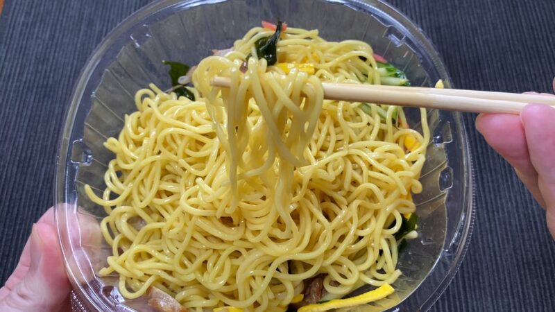 ファミマ冷やし中華を箸で持ち上げた様子。つやのある中華麺が醤油だれと具材に絡んでいる