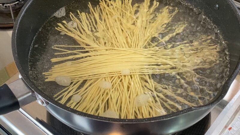 沸騰した鍋の中で、中華そばの乾麺が放射状に広がりながらゆでられている