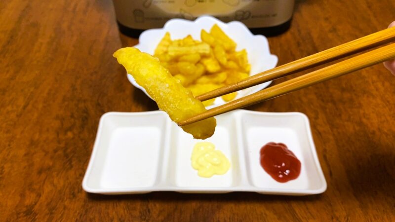 塩だけでシンプルに味わうためのフライドポテトを箸で持ち上げた場面。下にはケチャップとマヨネーズが並ぶ小皿