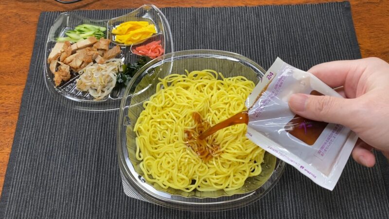 ファミマ冷やし中華の調理シーン。黄色い中華麺に醤油だれのスープをかけている