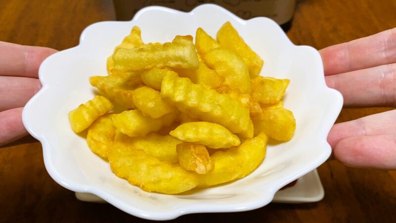 波型にカットされた業務スーパーのフライドポテトがたっぷり盛られた白い器を両手で支えている様子。