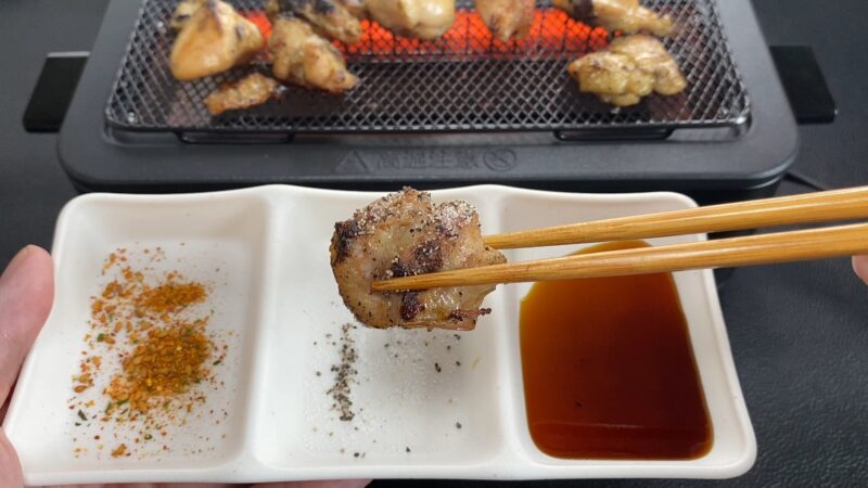 焼き鳥に塩をつけて食べる様子。手前には七味・胡椒・タレの3種が並ぶ白い小皿。
