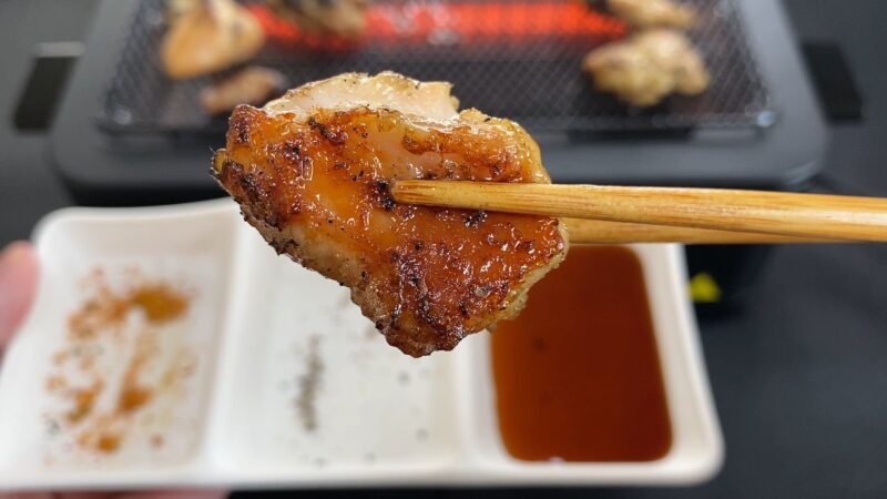 串なし焼き鳥をタレにくぐらせ、箸で持ち上げた瞬間のアップ。表面は香ばしく、照りがある。