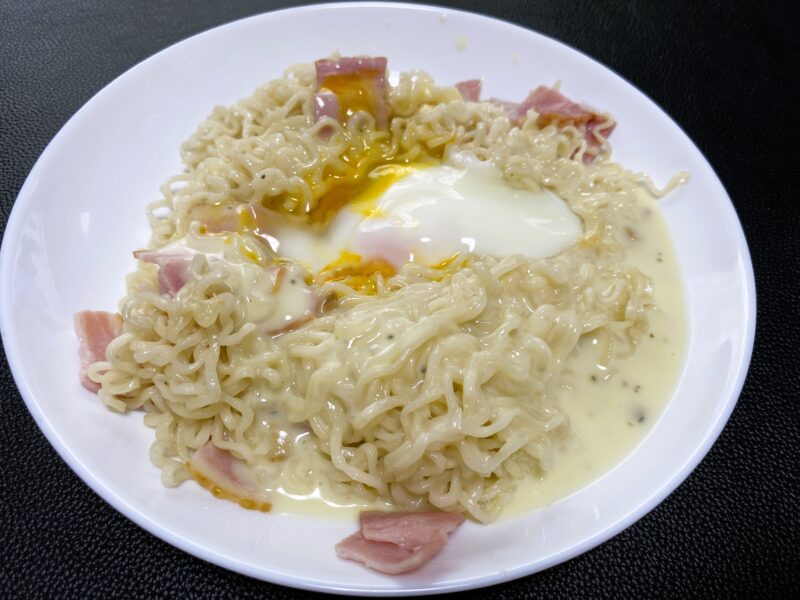 ベーコンと半熟卵をトッピングしたカルボナーラ風ノンフライ乾麺の全体写真。とろりとしたソースが麺に絡んでいる。