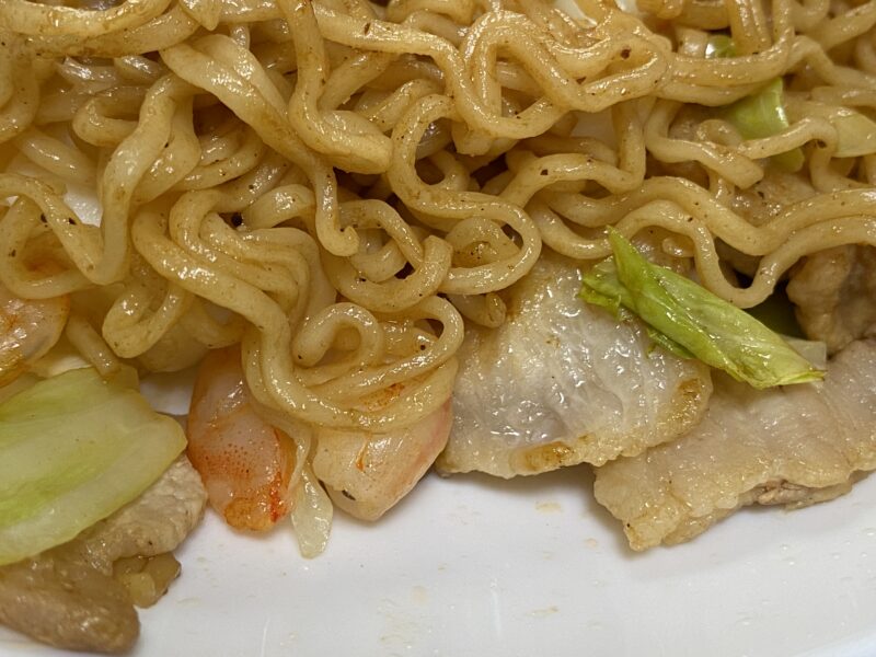 シーフード焼きそばの接写。縮れた平麺にソースがよく絡み、豚肉やキャベツ、エビが見える。