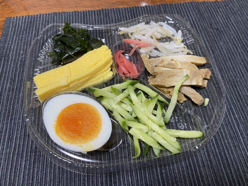 セブンイレブンの冷やし中華の具材(錦糸卵、ゆで卵、きゅうり、もやし、焼豚、紅しょうが、わかめ)をトレイに並べた状態。