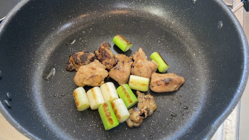 備長炭で焼いた串なし焼き鳥とカットした長ねぎをフライパンで焼いている様子。表面に焼き色がつき始めている。