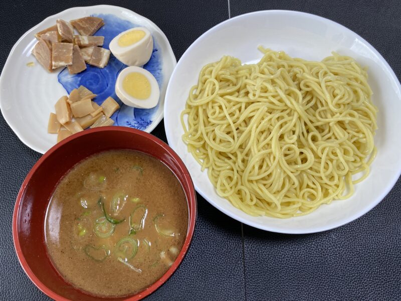 白い皿に盛られた中華麺と、別皿のチャーシュー、味玉、メンマ。赤い椀に入った濃厚なつけ汁が添えられた食欲をそそるつけ麺。