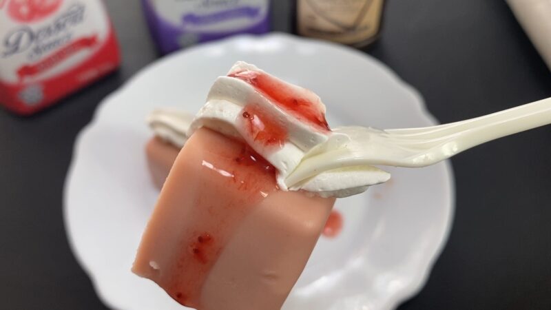 フォークで持ち上げたストロベリーチーズケーキにホイップクリームとストロベリーソースがかかっている