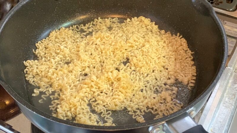 フライパンでマレーシア産ノンフライ乾麺を茹でている様子。水が少なく、麺がほぐれ始めている。