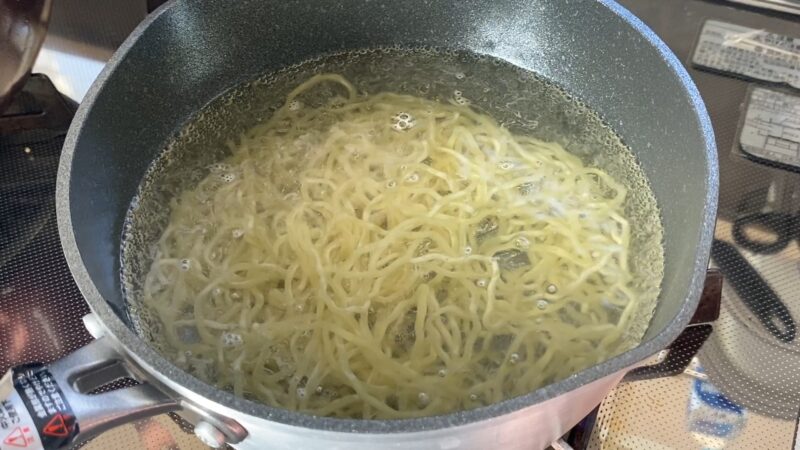 鍋で茹でられているウェーブ麺。お湯の中でほぐれ、麺がふっくらと広がっている。