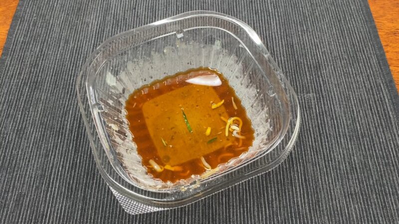 セブンイレブンの冷やし中華を食べ終えた後のスープ。具材のかけらが浮いている食後の状態。