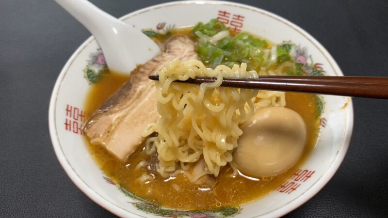 味噌ラーメンを箸で持ち上げた様子。チャーシューや煮卵、刻みねぎも盛り付けられている。