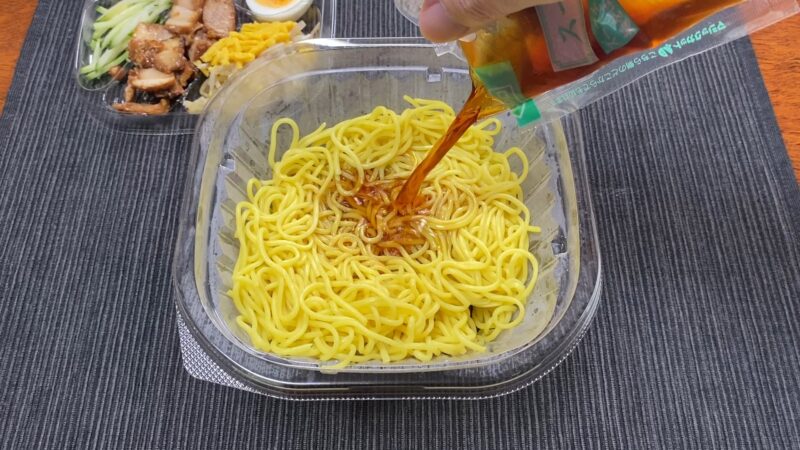 ローソン冷やし中華に醤油だれをかける瞬間。コンビニならではの本格的な中華麺が食欲をそそる