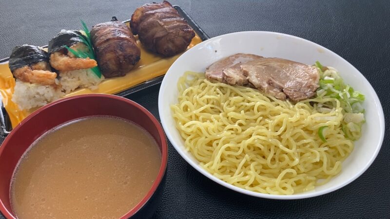 チャーシューと刻みネギを添えた冷やしつけ麺、つけ汁、寿司（えび天むすと肉巻きおにぎり）のセット