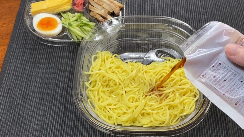 セブンイレブンの冷やし中華。麺の上に添付スープをかけている調理中の様子。具材は別トレイに分けられている。