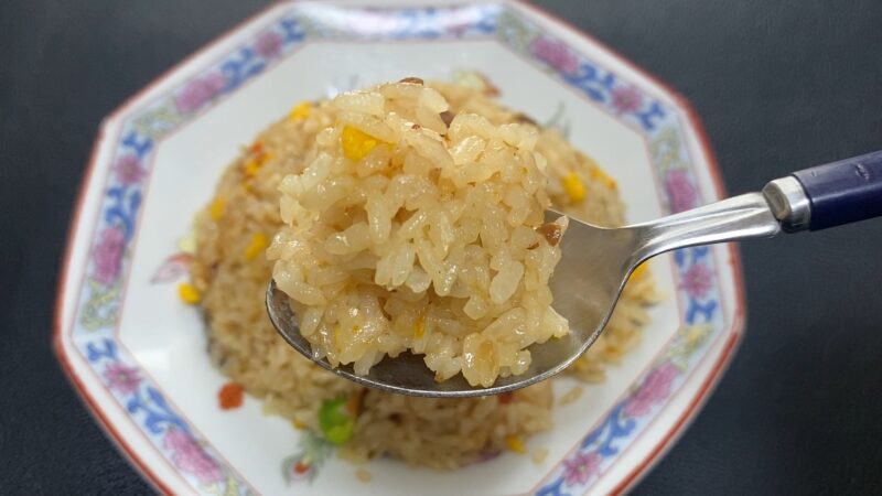 にんにくチャーハンをスプーンですくった状態。背景には器に盛られた全体がぼんやりと見える。