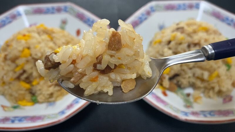 電子レンジで加熱したチャーハンをスプーンですくった写真。後ろに盛り付けられた皿が見える。