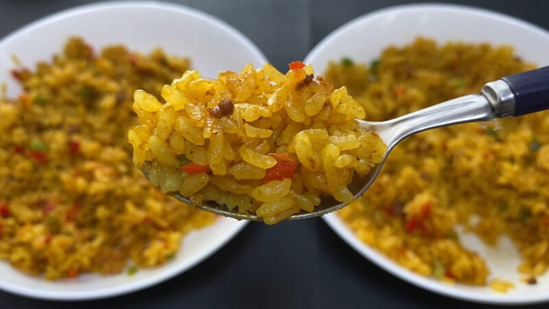 電子レンジで調理したドライカレーをスプーンですくったアップ写真。奥には白い皿に盛られたドライカレーが2皿並んでいる