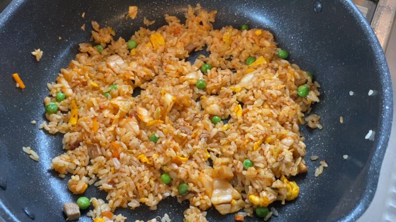 キムチを加えて炒めたチャーハン。フライパンの中で赤みが増し、グリンピースや卵も見える。