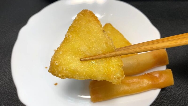 揚げた業務スーパーのチーズポテト。三角形の衣がきつね色にカリッと揚がり、箸で持ち上げられている。