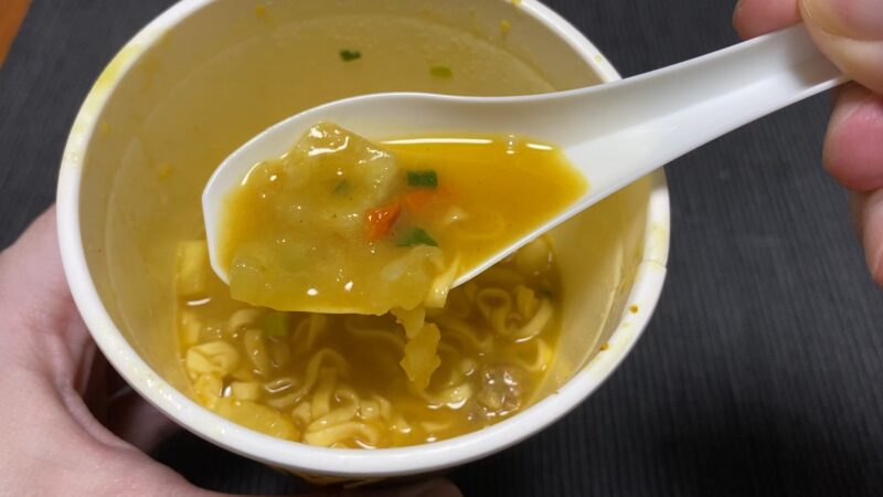 魔改造カップヌードル「ガリマヨカレー味」のスープをレンゲですくった写真。ポテトと人参が見える