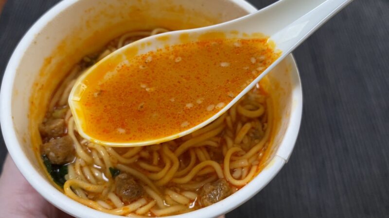 レンゲで掬ったファミマ担々麺のスープ、赤いラー油が浮かんでいる