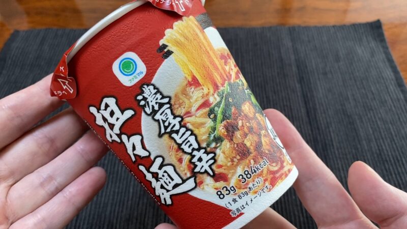 手に持ったファミマ「濃厚旨辛担々麺」のカップパッケージ