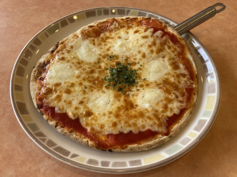 Wチーズで注文したサイゼリヤのマルゲリータピザ。とろけたチーズに焼き目がつき、中央にはパセリが振られている。お皿の上にピザカッターが添えられている。