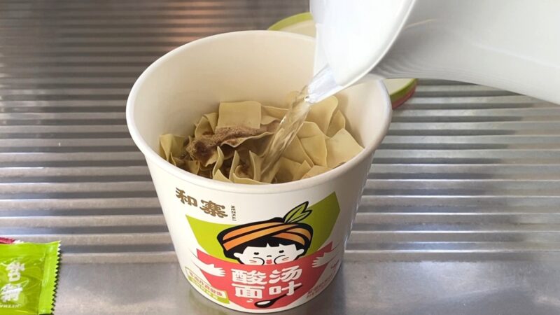 カップに麺と粉末スープを入れ、お湯を注いでいる様子。調理中の酸湯面叶