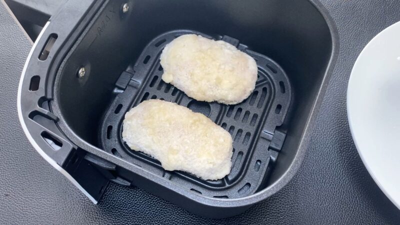 ノンフライヤーのバスケットに凍ったままの「肉厚 極旨とんかつ」を2枚並べた写真。白いパン粉が付き、調理前の状態がわかる。