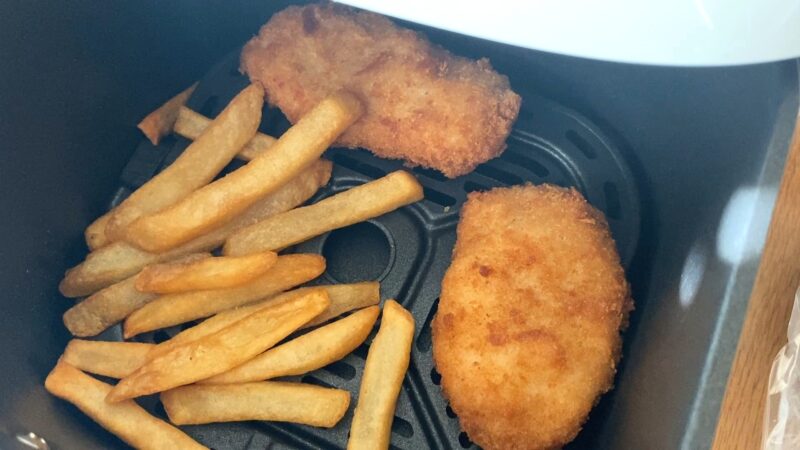 ノンフライヤーのバスケットで業務スーパー「肉厚 極旨とんかつ」とフライドポテトを一緒に加熱している様子。冷めた豚カツをノンフライヤーで温め直しを行うとサクサクで美味しさアップ。
