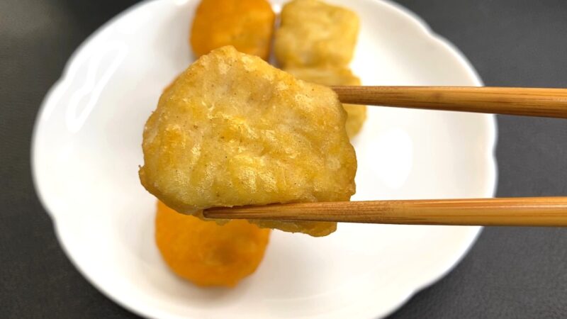 油で揚げたチキンナゲットを箸で持ち上げた様子。衣がカリッときつね色に揚がっている。