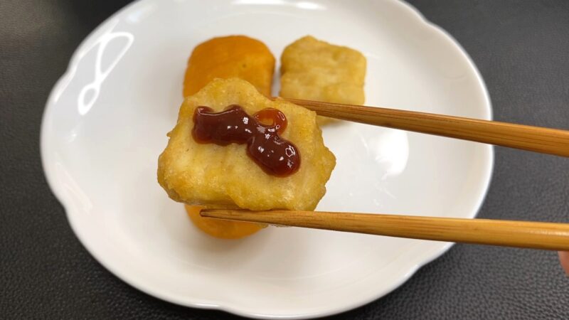 バーベキューソースをかけたチキンナゲット。甘辛いソースが表面に広がり、箸で持ち上げている。