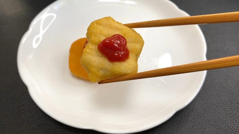 ケチャップをのせたチキンナゲット。赤いソースの色が映えて、箸で持ち上げた様子。