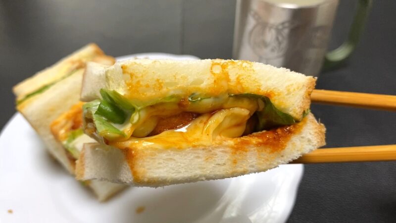 チキンナゲットサンドを箸で持ち上げた様子。レタスとソースがとろけて、断面からチーズが見える。