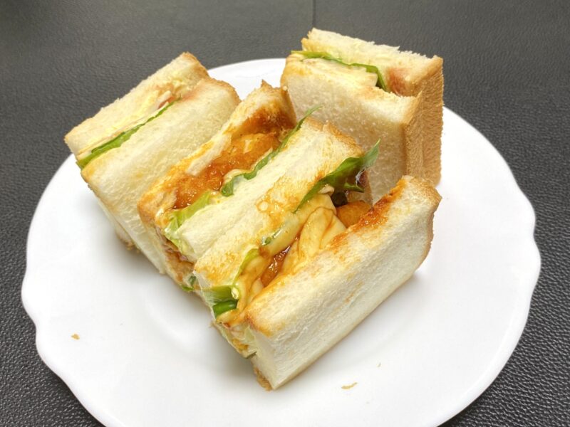 チキンナゲットをレタスと一緒にサンドしたサンドイッチ。バーベキューソースとマヨネーズがパンからのぞいている。