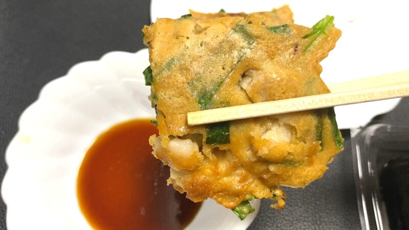 焼き上がったチヂミを箸でつまみ、たれにつけようとしている様子。中の豚肉が見えて美味しそう。
