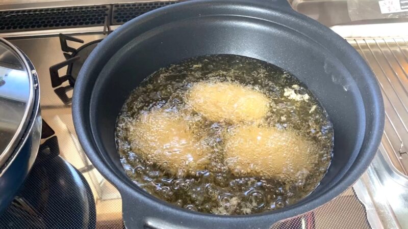 鍋で業務スーパー「肉厚 極旨とんかつ」を170℃の油で揚げている様子。油の中で泡が立ち、衣がふくらみながらきつね色に変化している。