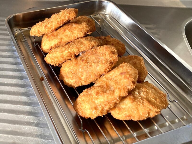 揚げたての業務スーパー「肉厚 極旨とんかつ」をバットの上で油を切っている写真。衣がこんがりと色づき、サクサクした質感が見てわかる。