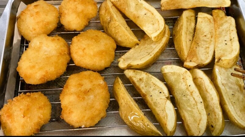 揚げたての「鶏屋さんのチキンカツ」とポテトを網の上に並べて冷ましている様子。衣は黄金色で、香ばしい揚げ上がりが見て取れる。