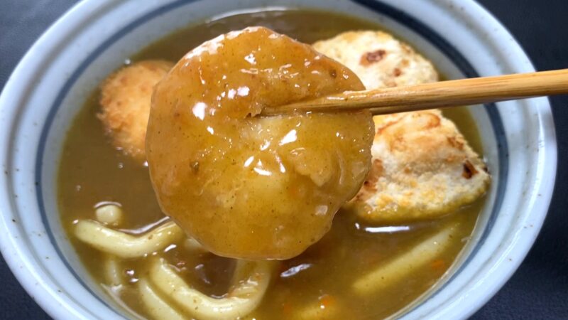 カレーうどんの中からチキンカツを箸で持ち上げた様子。とろみのあるルーが衣に絡み、艶やかな仕上がり。