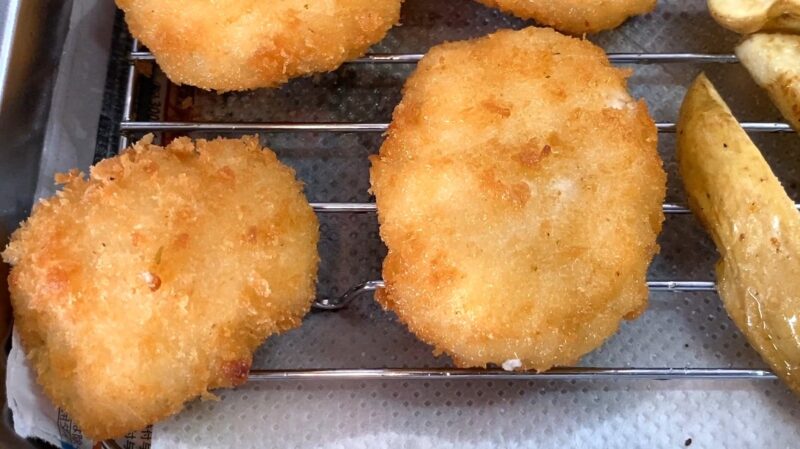 揚げたての「鶏屋さんのチキンカツ」を網の上で冷ましている様子。衣が黄金色に揚がり、サクサク感が伝わる見た目。
