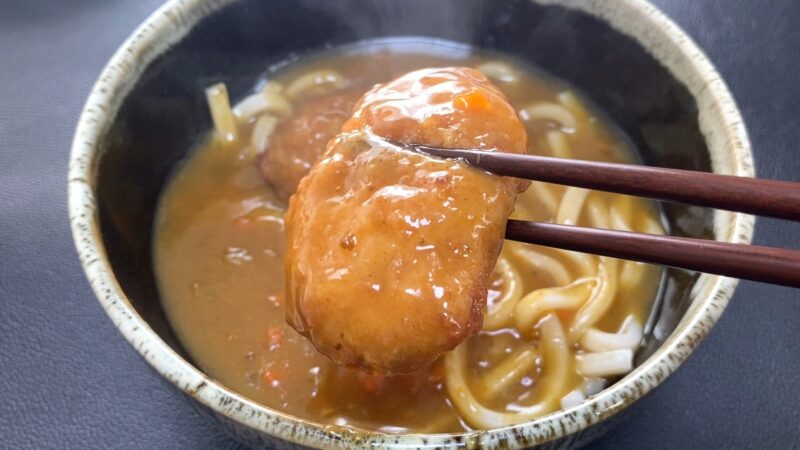 カレーうどんの中から業務スーパー「肉厚 極旨とんかつ」を箸で持ち上げた写真。衣がカレーをまとって艶やかに輝き、食欲をそそる仕上がり。