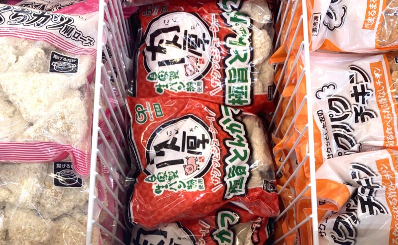 業務スーパーの冷凍食品コーナーに並ぶ「肉厚 極旨とんかつ」の赤いパッケージ。左にピンクの肩ロースカツ、右にオレンジのチキン商品が陳列されている。