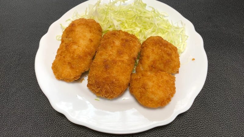 揚げた業務スーパー「肉厚 極旨とんかつ」をキャベツの千切りと一緒に皿に盛り付けた写真。衣がこんがりと色づいている。